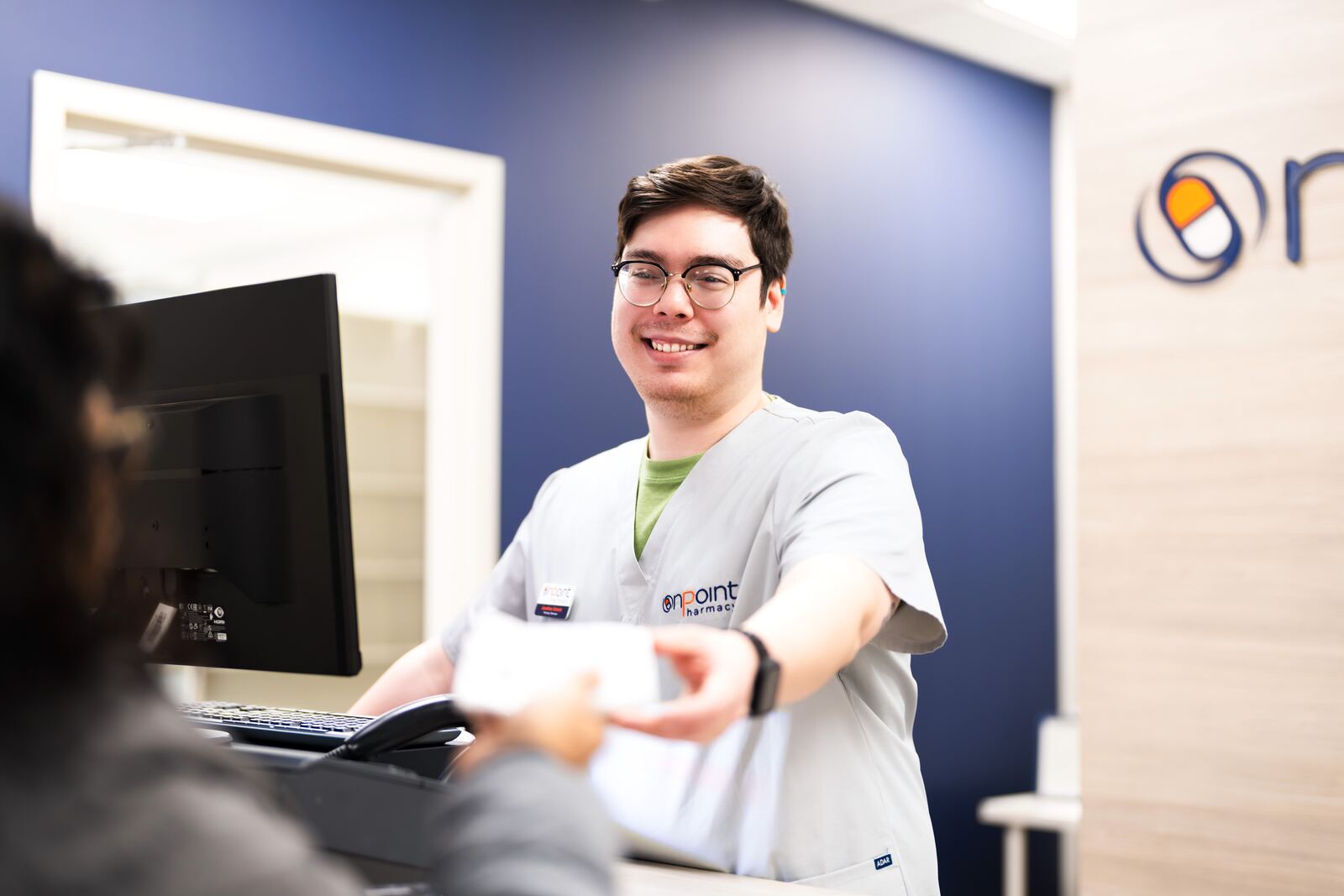 An OnPoint pharmacist handing a patient their prescription at the counter